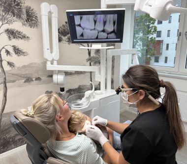 Zahnärztin untersucht ein Kind auf dem Schoß der Mutter im Behandlungszimmer.