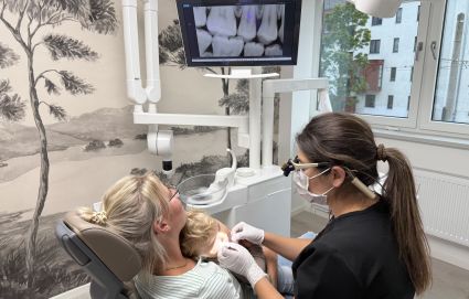 Zahnärztin untersucht ein Kind auf dem Schoß der Mutter im Behandlungszimmer.