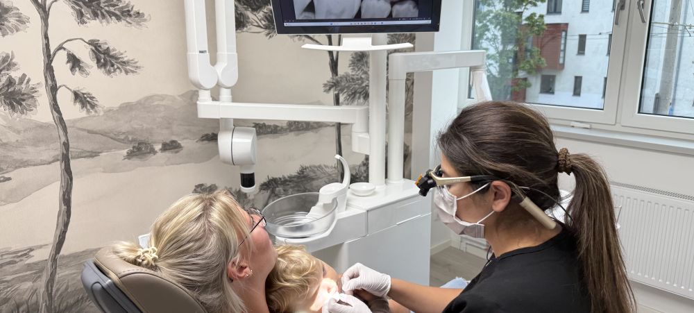 Zahnärztin untersucht ein Kind auf dem Schoß der Mutter im Behandlungszimmer.